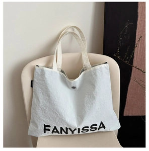 Detail of silver snap button and black FANYISSA logo on a light blue tote bag