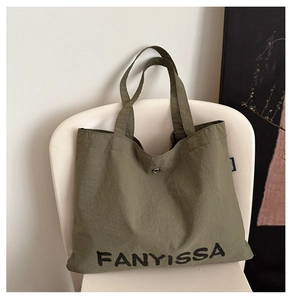 Detail of olive green tote bag with brand logo and snap button on a white chair