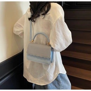 Détail du sac bandoulière bleu pervenche avec texture tressée sur chemise en lin blanc