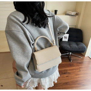 Détail du sac beige avec rabat tissé ondulé et corps en cuir dans une pièce cosy