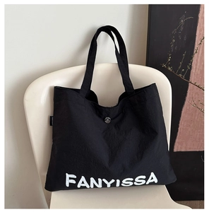 Detail of black tote bag featuring white FANYISSA lettering and silver magnetic closure