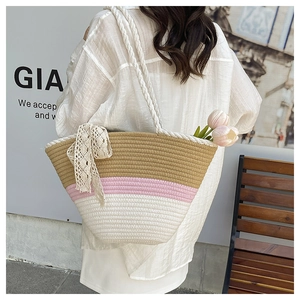 Detail of a tricolor woven straw tote with white lace bow and rope handles worn by model