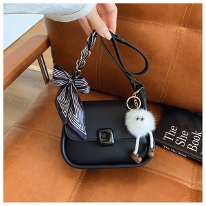 Detail of black crossbody bag with striped silk scarf and plush doll charm on sofa
