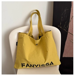 Detail of yellow nylon tote bag featuring black FANYISSA print and secure metal snap closure