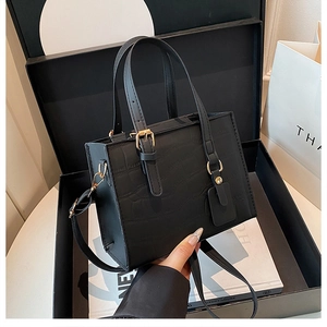 Detail of black crocodile texture handbag with gold hardware in a gift box setup