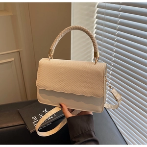 Détail du sac beige avec rabat ondulé et poignée tressée sous une lumière douce et élégante