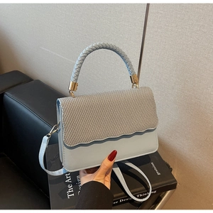 Détail du sac bleu clair avec rabat scintillant et poignée tressée sur un livre