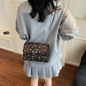 Sac bandoulière noir chic avec imprimé cerises et chaîne porté par un mannequin