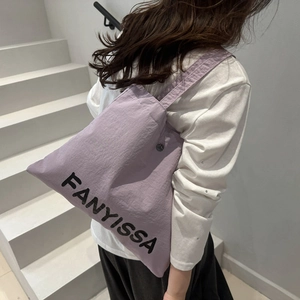 Light purple nylon tote bag with black letter print worn by a model on white stairs