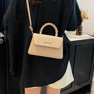 Sac bandoulière beige avec poignée torsadée et fermoir en métal porté par un mannequin