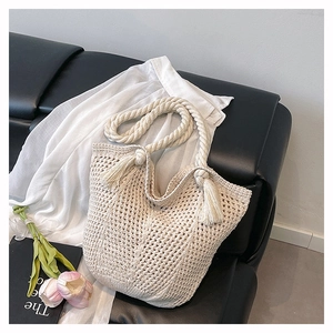 Detail of off-white hollow woven crochet tote bag with tassel on a leather sofa