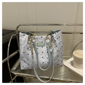 Détail du sac fourre-tout bleu clair matelassé avec nœuds noirs et logo doré sur étagère