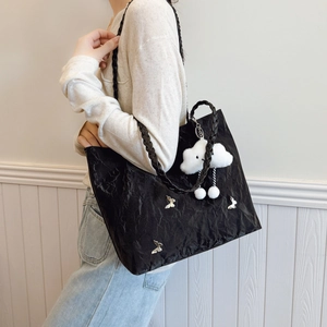 Minimalist black tote bag with butterfly charm and woven straps on white background
