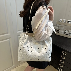 Sac fourre-tout blanc à motif nœuds noirs et anneaux dorés porté à l'épaule