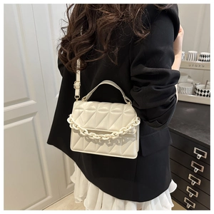 Détail du sac beige matelassé avec chaîne épaisse porté par un mannequin en intérieur