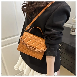 Sac bandoulière marron matelassé avec chaîne décorative en résine porté par un modèle
