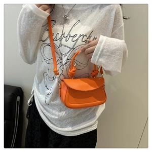 Detail of orange leather crossbody bag with knot handle and flap closure worn by model