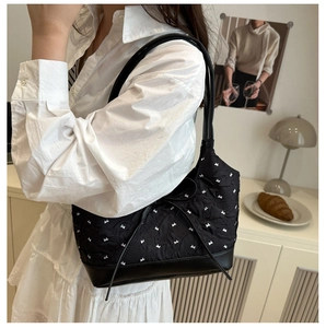 Détail du sac à bandoulière matelassé noir avec motif nœud blanc et fond en cuir