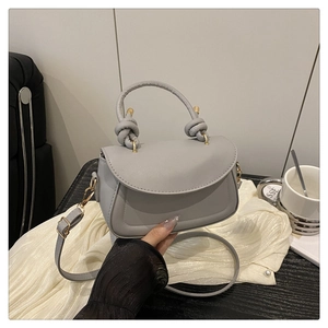 Close-up of light grey shoulder bag with unique knot handle detail on a dark wooden table