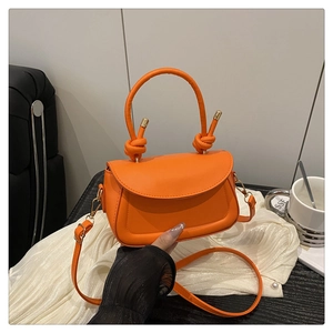 Detail of bright orange crossbody bag featuring knotted handles and gold hardware