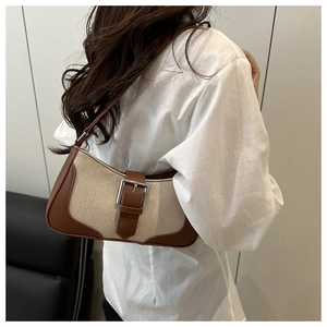 Shoulder bag detail featuring beige canvas with brown leather trim and silver buckle strap