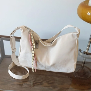 Detailed close-up of beige suede hobo bag with colorful knot charm on a glass table