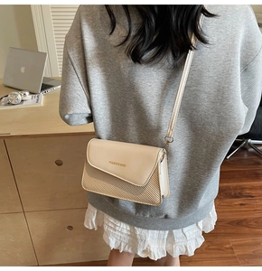 Detail of a chic cream crossbody bag featuring a leather flap and woven texture stitching