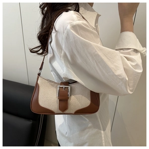 Detail of beige canvas and brown leather baguette bag with silver buckle worn by a model