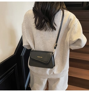 Detail of a black crossbody bag with asymmetric flap and carbon fiber texture