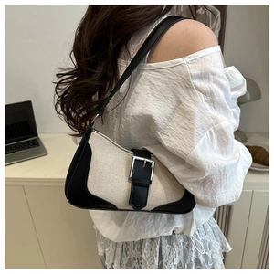 Detail of canvas baguette bag with black leather trim and silver metal buckle on model