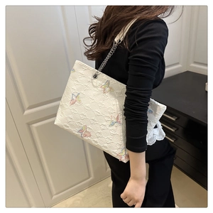 Detail of white tote bag featuring colorful butterfly embroidery and metal chain strap