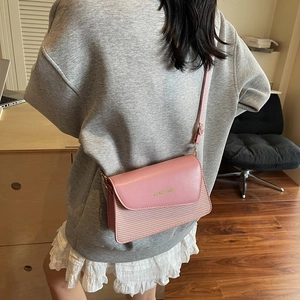 Pink crossbody bag with woven texture and wide strap shown on a model in a cozy room