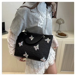 Detail of black tote bag with colorful butterfly embroidery and metal chain strap