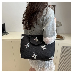 Close-up of black quilted tote bag featuring colorful butterfly embroidery and chain strap