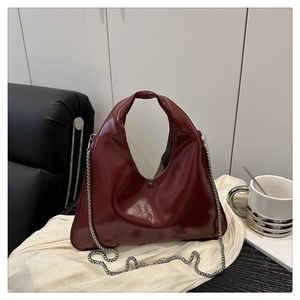 Detail of wine red hobo bag in high-gloss patent leather with sleek metal chain strap