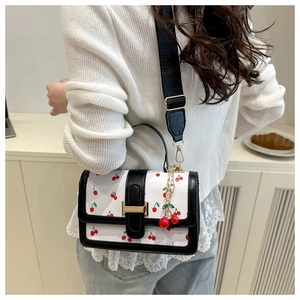 Close-up of a white crossbody bag with cherry prints and black leather trim detail