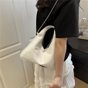 Minimalist white patent leather crescent shoulder bag with silver chain strap worn by model