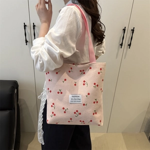 Pink corduroy tote bag with cherry patterns and shoulder strap shown on a model