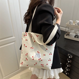 Off-white canvas tote bag with red cherry print shown on a model in a minimalist setting