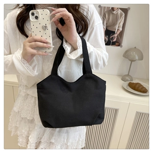 Minimalist black canvas tote bag being held by a woman in a lifestyle home setting