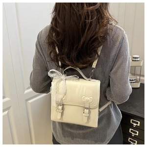 Detail of cream leather backpack featuring lace bow charm and polished metal buckles