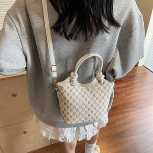 Sac seau chic avec motif vintage et garniture dorée, porté en bandoulière élégante