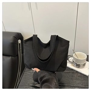 Close-up of a minimalist black canvas tote bag being held to show its compact size