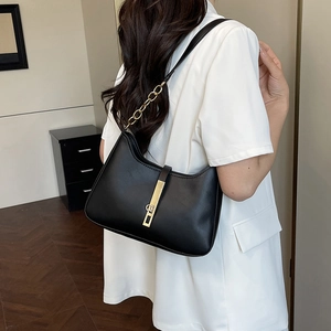 Sac sous le bras minimaliste en cuir noir avec détails dorés porté par un mannequin