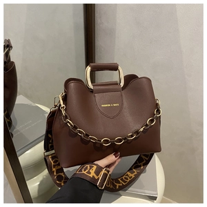 Detail of dark brown leather handbag with metal chain and geometric pattern wide strap