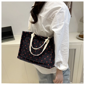 Detail of black corduroy tote bag with red heart patterns and shoulder strap detail