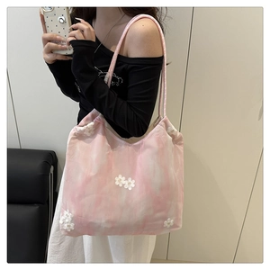 Detail view of pink mesh tote bag with white floral embroidery worn by a model