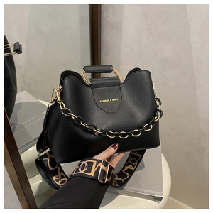 Detail of black leather bucket bag with gold metal handle and patterned fabric strap