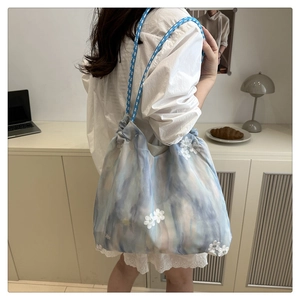 Detail of blue tie-dye drawstring bag featuring 3D white floral embroidery and mesh fabric