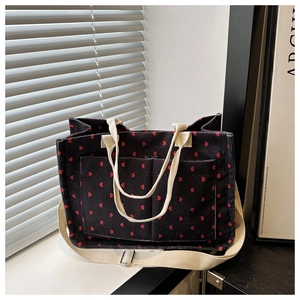 Detail of dark corduroy tote bag featuring red heart patterns and dual front pockets
